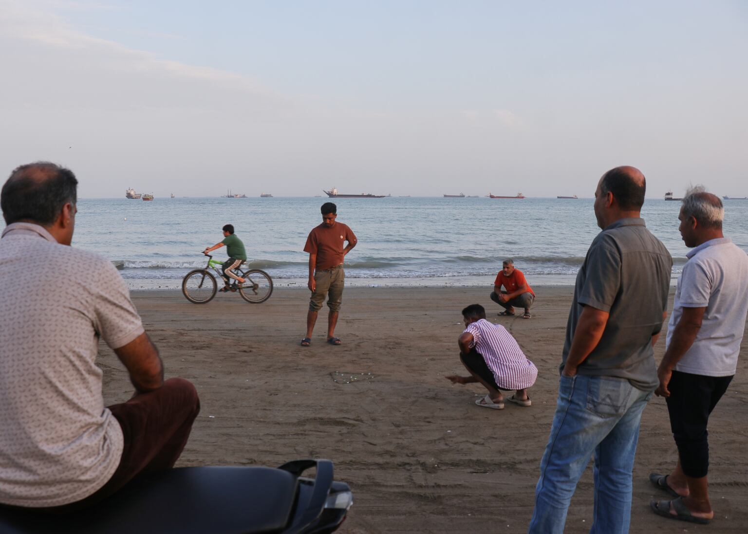 Men gather along the shore as a mix of bulk carriers, cargo ships and service vessels line the horizon in the Strait of Hormuz off Bandar Abbas, Iran (Razieh Poudat/AP)