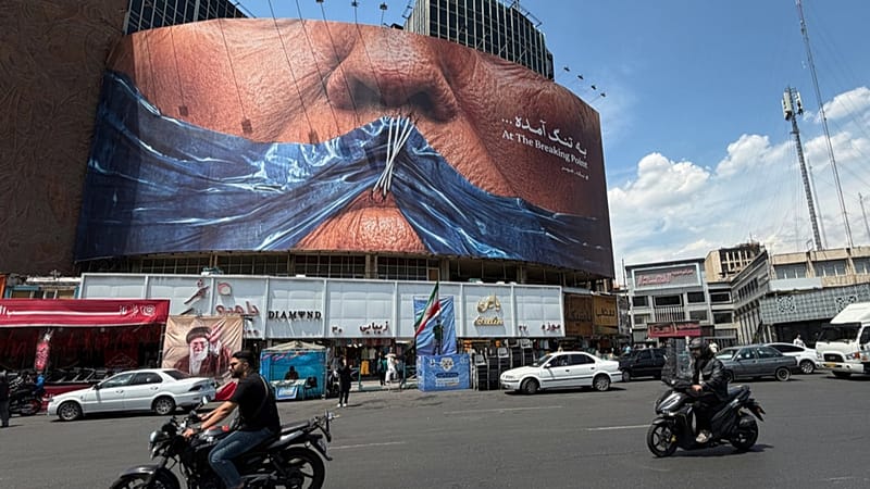 Vehicles drive past a billboard with graphic showing Strait of Hormuz and sewn lips of US President Donald Trump in a square in downtown Tehran, Iran, Saturday, May 2, 2026